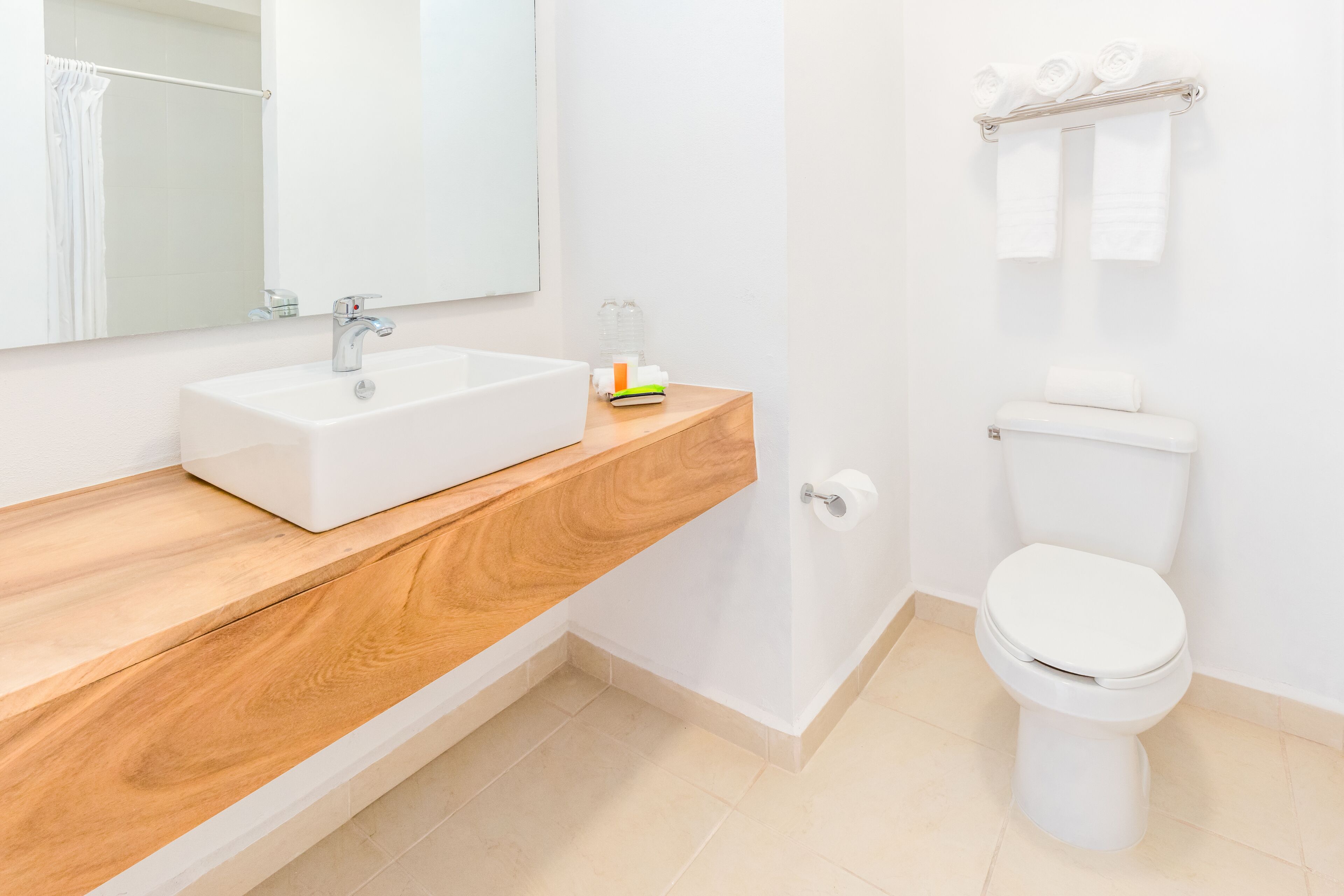 Un baño moderno con un lavamanos blanco, tocador de madera, inodoro y un perchero para toallas.