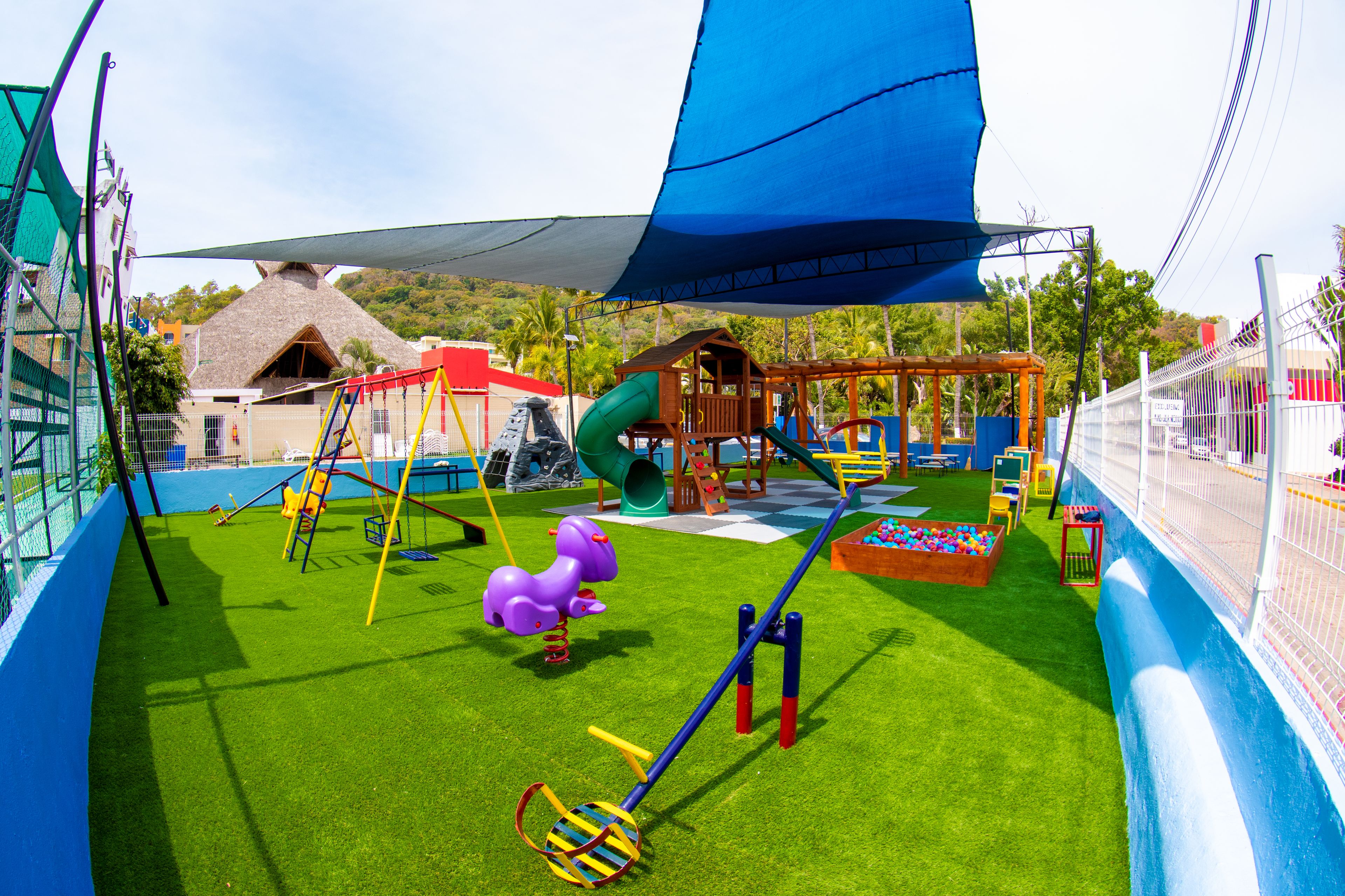 A playground with various play equipment, including slides and swings, surrounded by a fenced area.