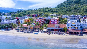 Un pueblo costero con edificios de colores, una playa con sombrillas y montañas al fondo.