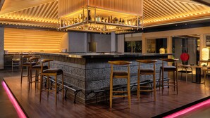A bar area with a central island, bar stools, and a variety of bottles. - Mövenpick Resort & Spa Bintan Lagoon (Bintan)