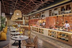 A restaurant with a long counter, multiple tables, and chairs. There are shelves with dishes and bottles on the counter. - Mövenpick Resort & Spa Bintan Lagoon (Bintan)