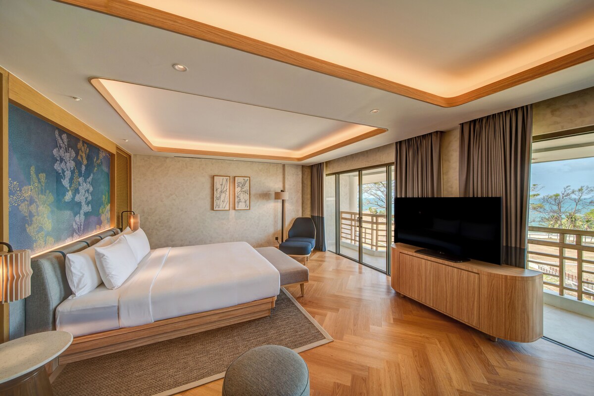 A modern hotel room with a large bed, a TV, and a balcony with a view.