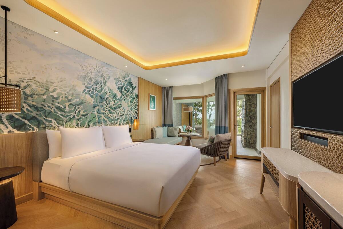 A hotel room with a large bed, a desk, a chair, a TV, and a mural on the wall.
