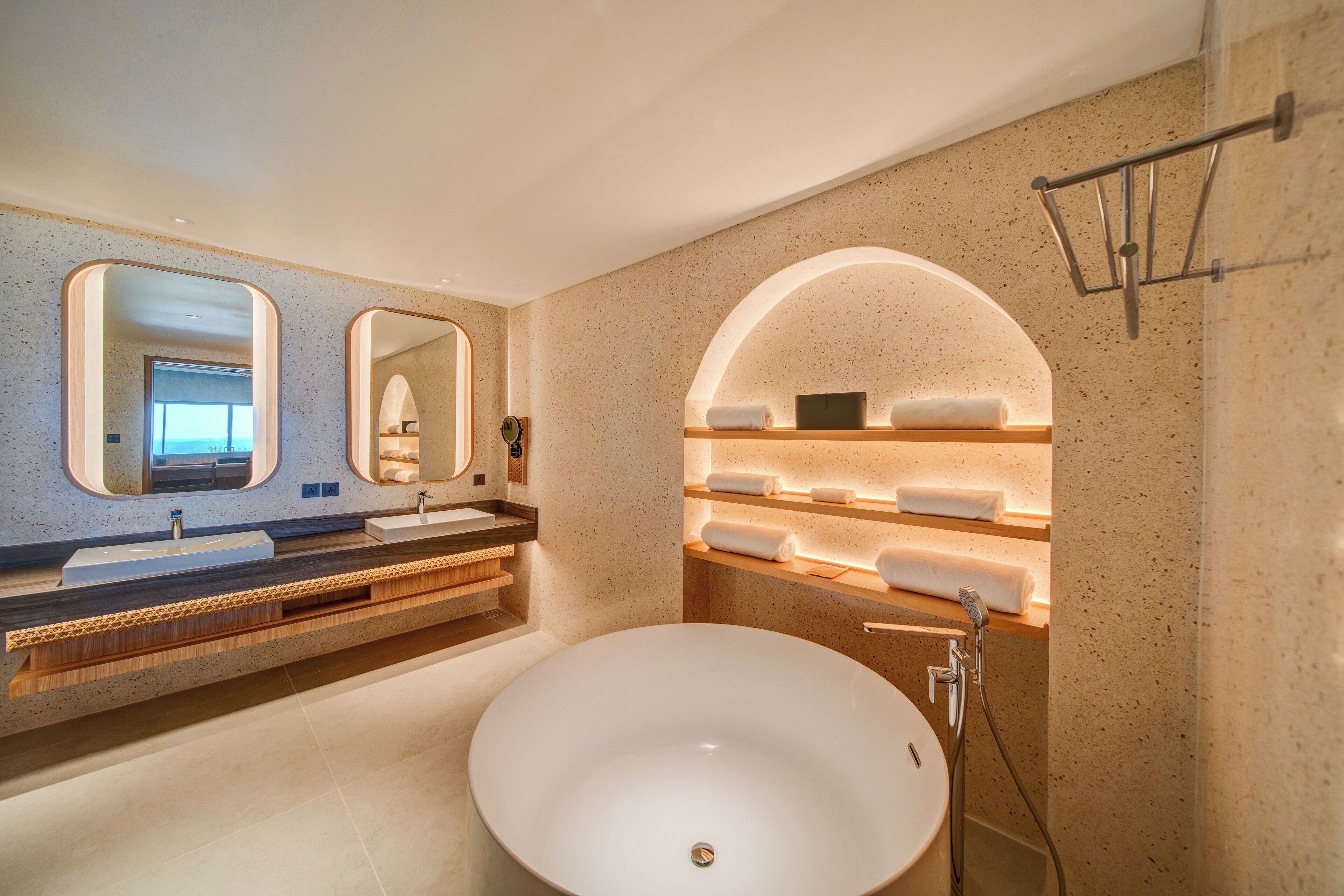 A modern bathroom with a large freestanding sink, dual mirrors, and built-in shelves with towels.