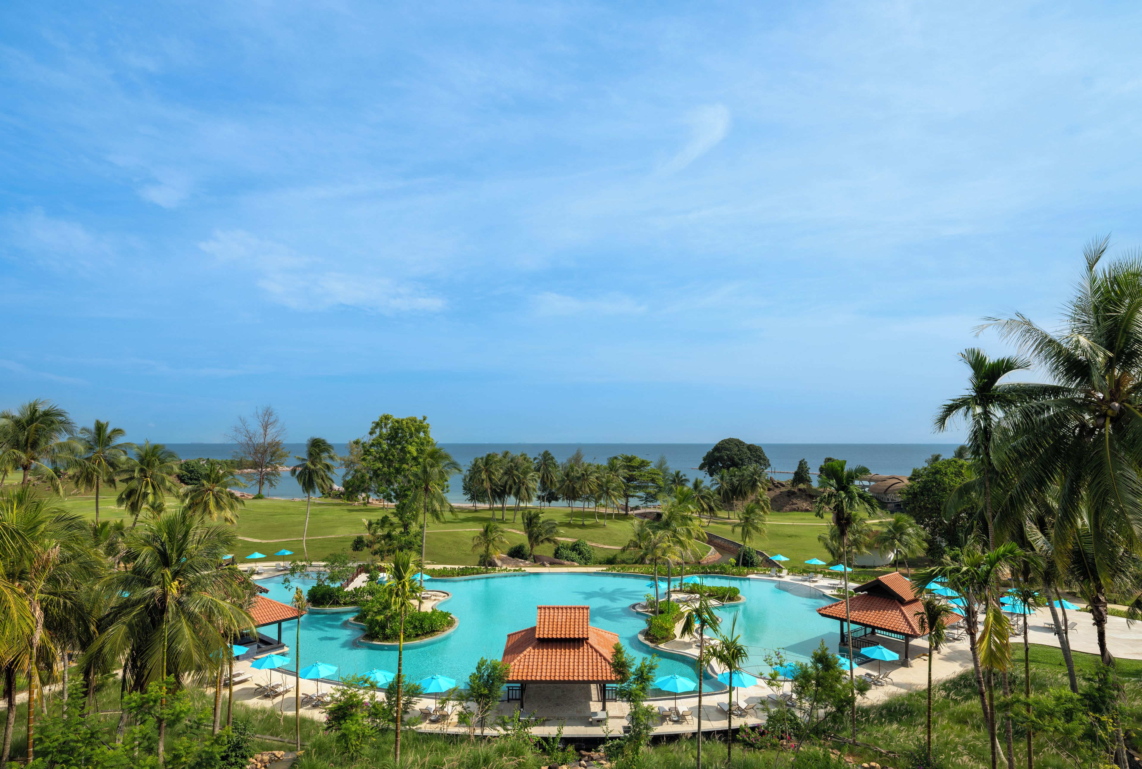 A resort with multiple swimming pools, palm trees, and a view of the ocean.