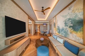 A modern living room with a flat-screen TV, wooden furniture, a ceiling fan, and a floral wall mural. - Mövenpick Resort & Spa Bintan Lagoon (Bintan)
