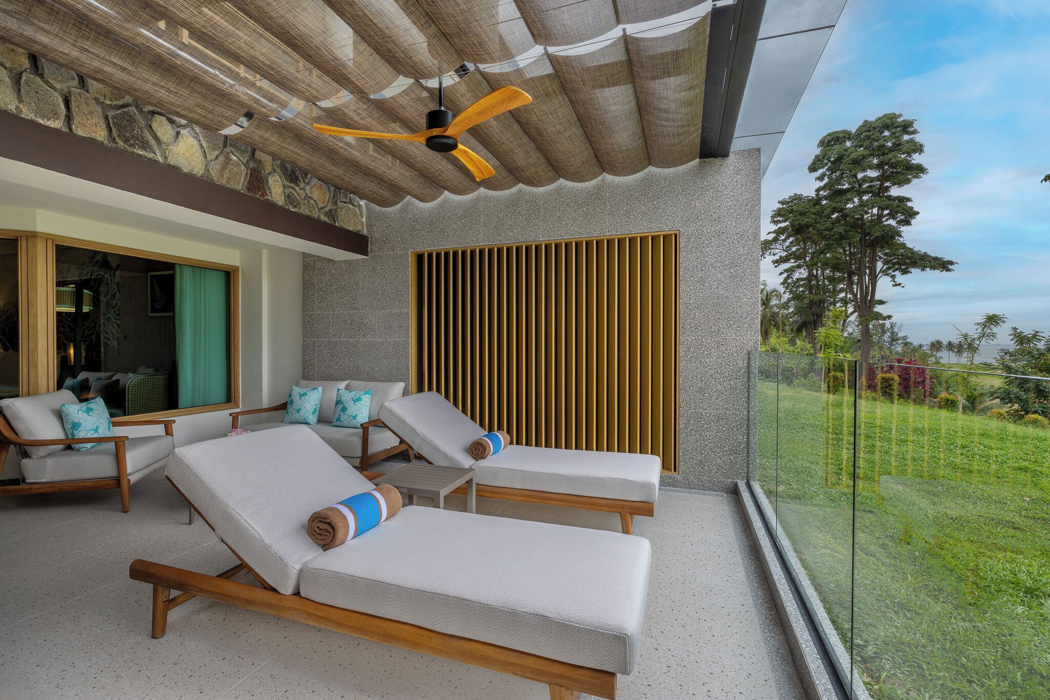 Un balcon avec des fauteuils de jardin, un ventilateur de plafond et une vue sur l’extérieur.