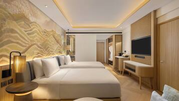 A modern hotel room with two beds, a TV, a desk, and a bathroom visible in the background.