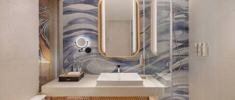 A modern bathroom with a glass shower enclosure, a wooden vanity, and a marble-patterned wall.
