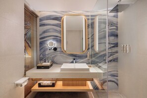 A modern bathroom with a glass shower enclosure, a wooden vanity, and a marble-patterned wall. - Mövenpick Resort & Spa Bintan Lagoon (Bintan)