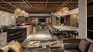 A modern dining area with a long table, multiple chairs, and hanging light fixtures. - Mövenpick Resort & Spa Bintan Lagoon (Bintan)