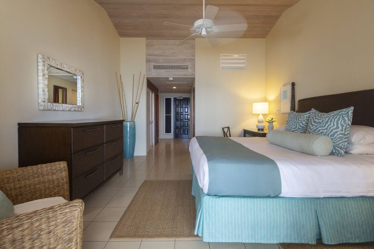 A bedroom with a bed, dresser, mirror, lamp, and a view of the hallway.