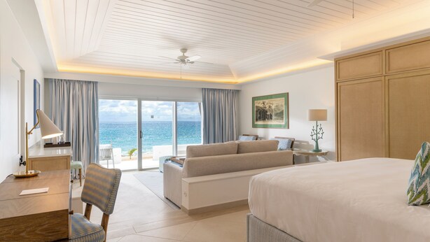 A hotel room with a bed, a sofa, a dining table, and a view of the ocean.