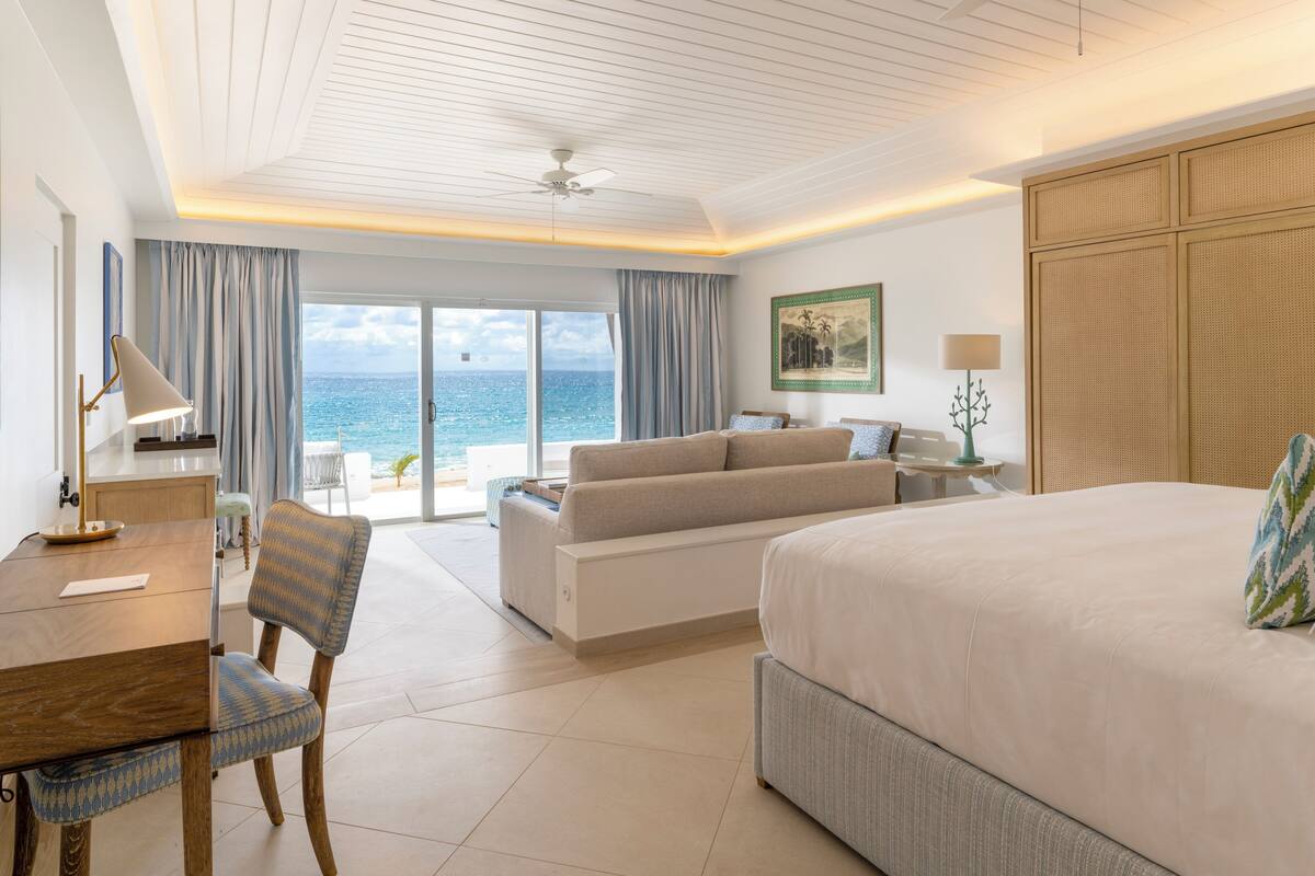 A hotel room with a bed, a sofa, a dining table, and a view of the ocean.