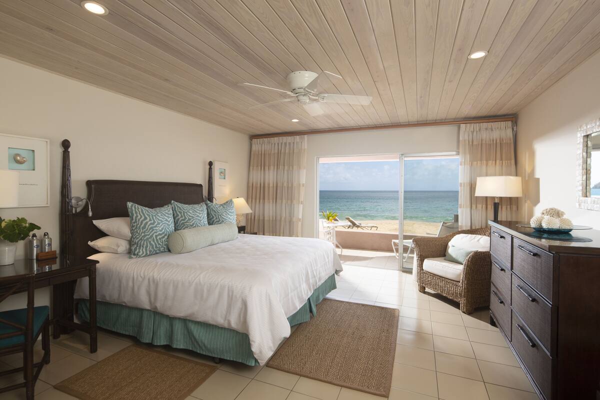 A bedroom with a large bed, a desk, a chair, a dresser, and a view of the ocean.