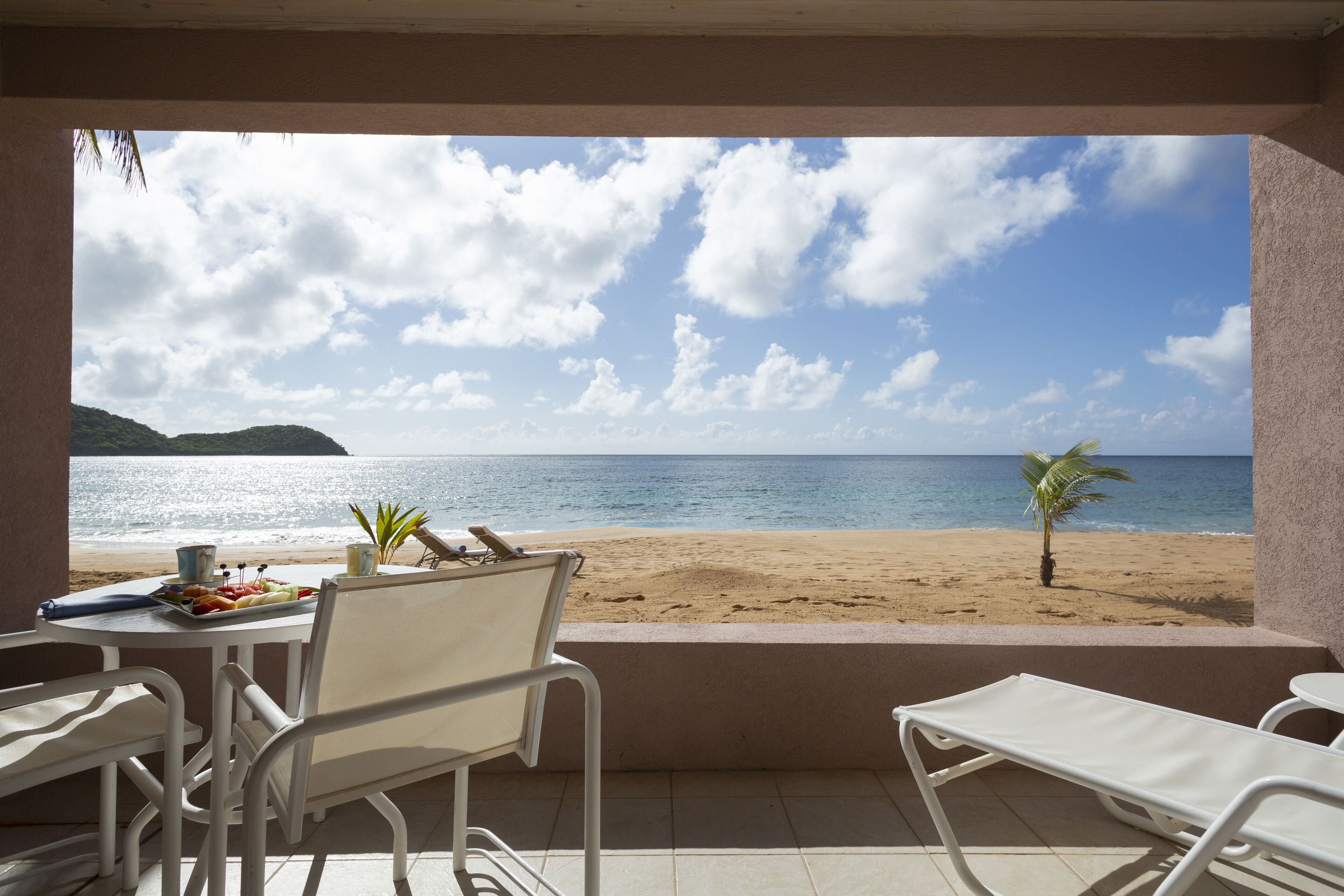 A balcony with a view of the beach, a table with a fruit platter, and a chair.