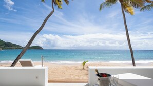 Une vue sur la plage avec un espace détente doté de chaises longues blanches, un seau contenant une bouteille et des verres, et un palmier.