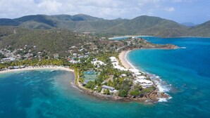 An aerial view of a coastal resort with a beach, clear turquoise waters, and lush greenery.