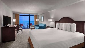 Ein Hotelzimmer mit einem großen Bett, einem Fernseher, einem Schreibtisch, einem Stuhl und einem Balkon mit Meerblick.