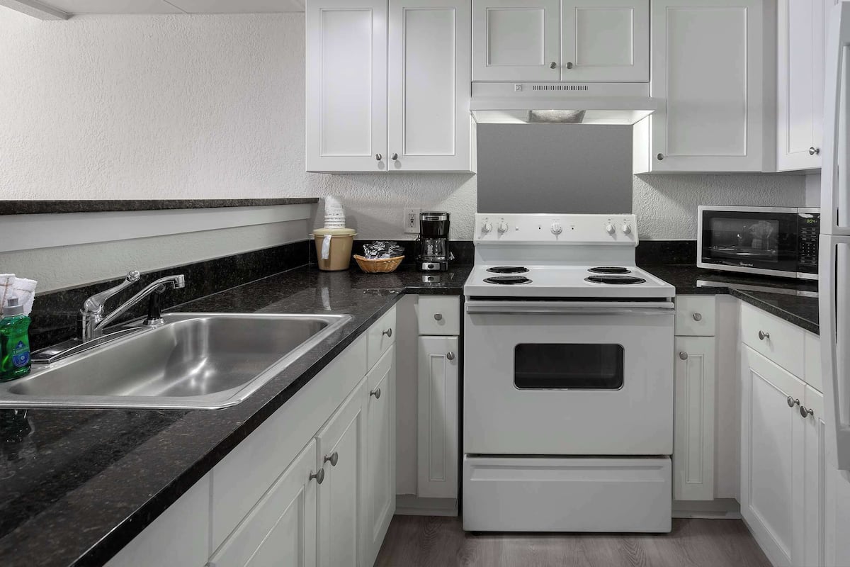 Una cocina moderna con armarios blancos, un lavamanos de acero inoxidable, un horno doble y un microondas.