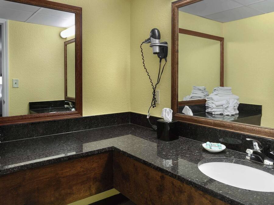Une salle de bain d’hôtel avec un comptoir en granit, un lavabo, un sèche-cheveux et un miroir.