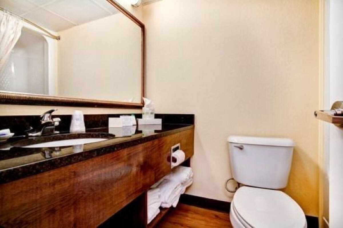 Un baño de hotel con tocador de madera, un lavamanos, un espejo, un inodoro y un perchero para toallas.