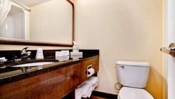 Un baño de hotel con tocador de madera, un lavamanos, un espejo, un inodoro y un perchero para toallas.