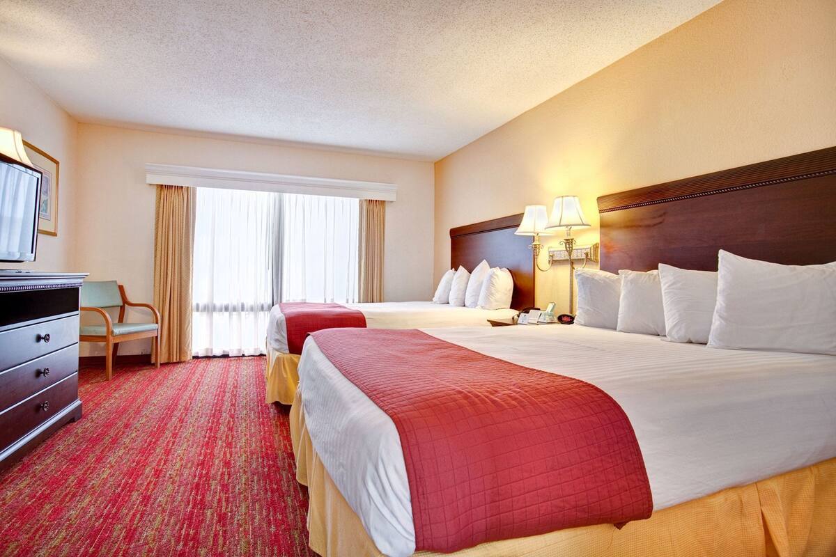 Una habitación de hotel con dos camas, un escritorio, una silla, un televisor y una ventana con cortinas.