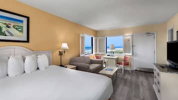A hotel room with a bed, a desk, a chair, a television, and a view of the beach.