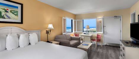 A hotel room with a bed, a desk, a chair, a television, and a view of the beach.