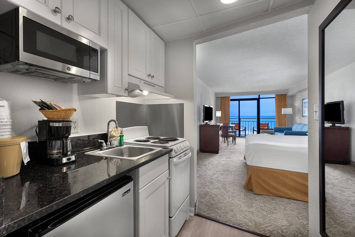 Una habitación de hotel con kitchenette, cama, televisor y balcón con vistas.