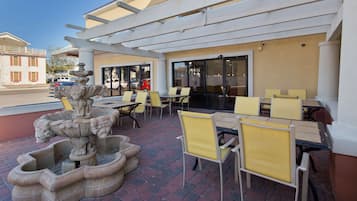 An outdoor patio with stone fountains, yellow chairs, and tables.