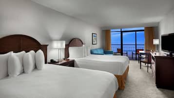 A hotel room with two beds, a desk, a television, and a balcony with a view.