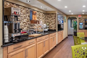 A hotel breakfast area with a coffee machine, food display, and seating. - Best Western Apalach Inn (Apalachicola)