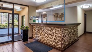 Et receptionområde med et moderne design, med en glasdisk, en mønstret væg og en stor glasdør, der fører udendørs.