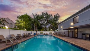 A swimming pool with lounge chairs, a brick deck, and a building with a white exterior.