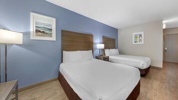 A hotel room with two beds, a nightstand, a lamp, and a framed picture on the wall.