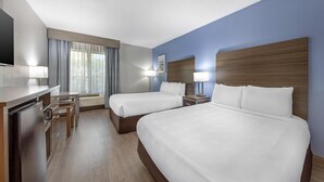 A hotel room with two beds, a desk, a refrigerator, and a window with curtains.