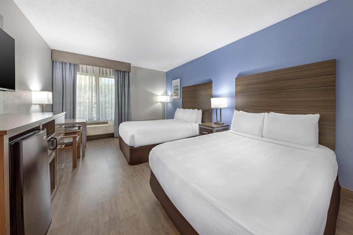 A hotel room with two beds, a desk, a refrigerator, and a window with curtains.