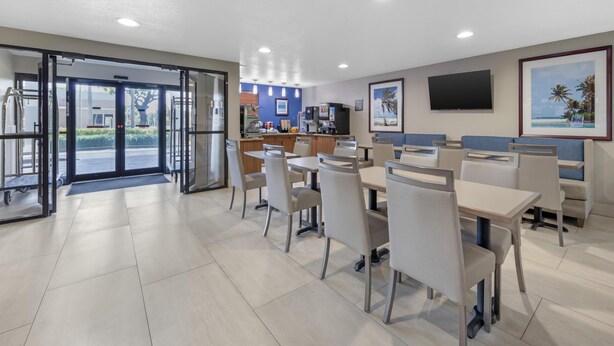A hotel dining area with tables and chairs, a reception desk, and a television on the wall.