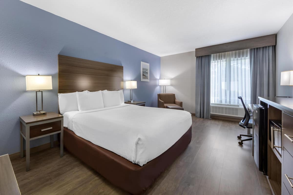 A hotel room with a large bed, bedside tables with lamps, a desk with a chair, and a window with curtains.