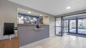 A reception area with a counter, a mounted TV, and a view of the outside through glass doors.