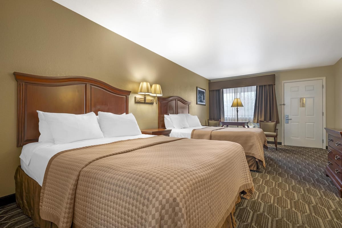 A hotel room with two beds, a desk, a chair, and a door.