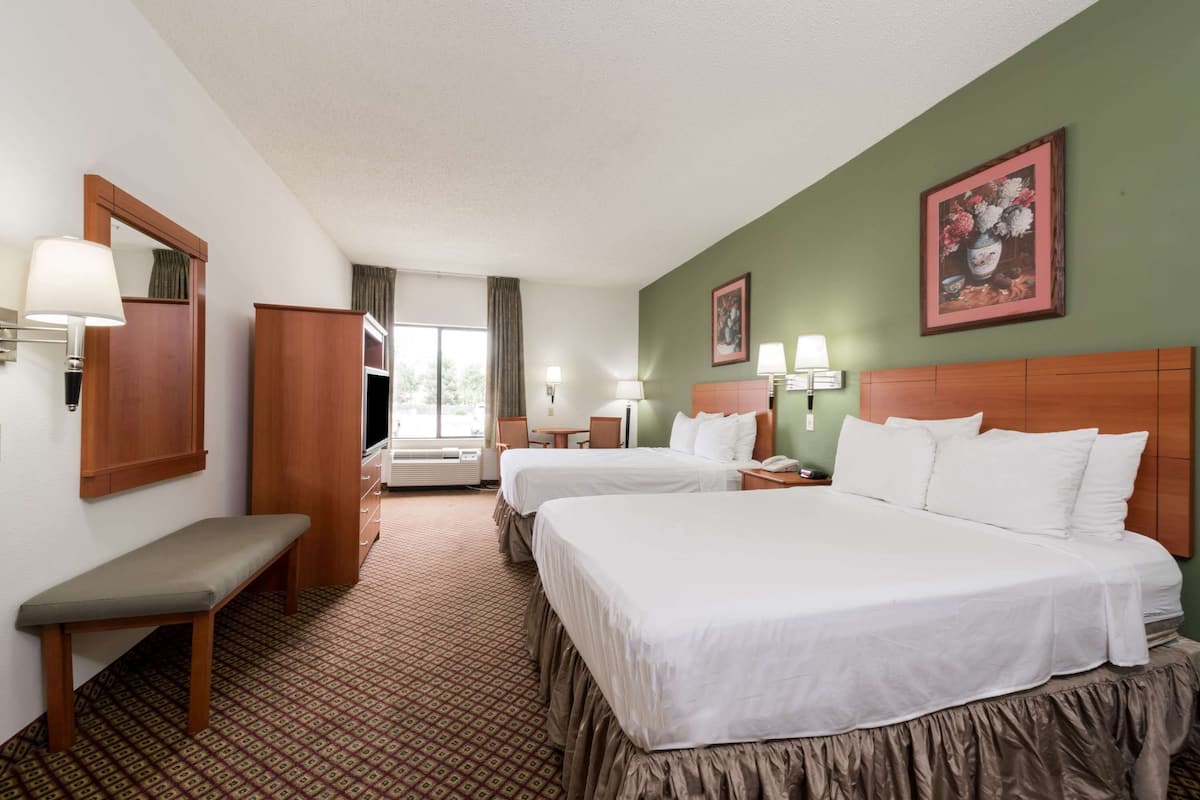 A hotel room with two beds, a bench, a desk, a chair, and a window with curtains.