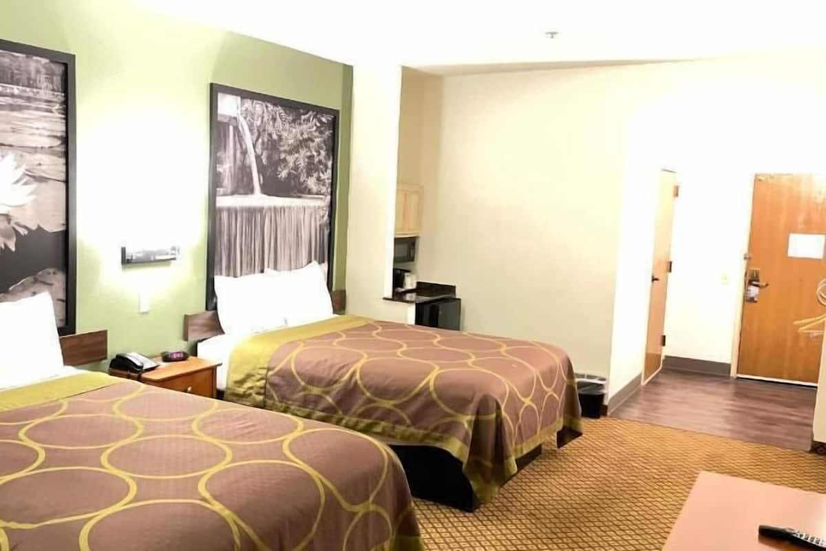 A hotel room with two beds, a desk, a chair, a TV, and a door.