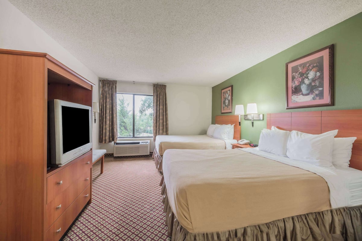 A hotel room with two beds, a television, a desk with a lamp, and a window with curtains.