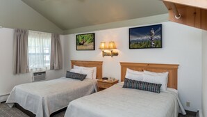 A hotel room with two beds, a window with curtains, a wall-mounted lamp, and two framed pictures. - Rivers Edge Resort (Fairbanks)