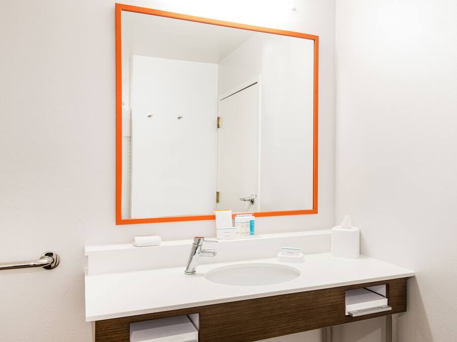 Une salle de bain avec un lavabo blanc, un miroir avec un cadre orange et un porte-serviettes.
