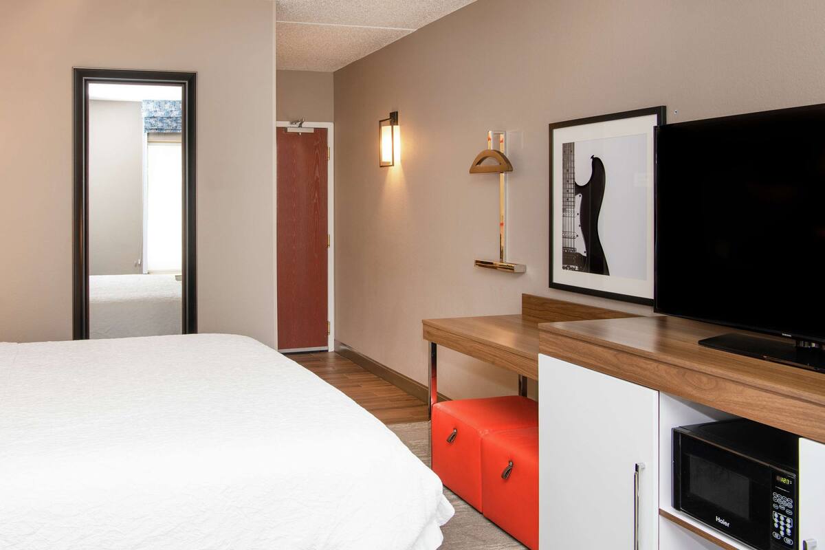 Une chambre d’hôtel comprenant un lit, un bureau avec une télévision, un four à micro-ondes et un meuble de rangement rouge.