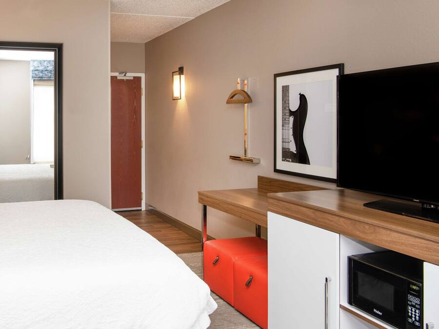 Une chambre d’hôtel comprenant un lit, un bureau avec une télévision, un four à micro-ondes et un meuble de rangement rouge.